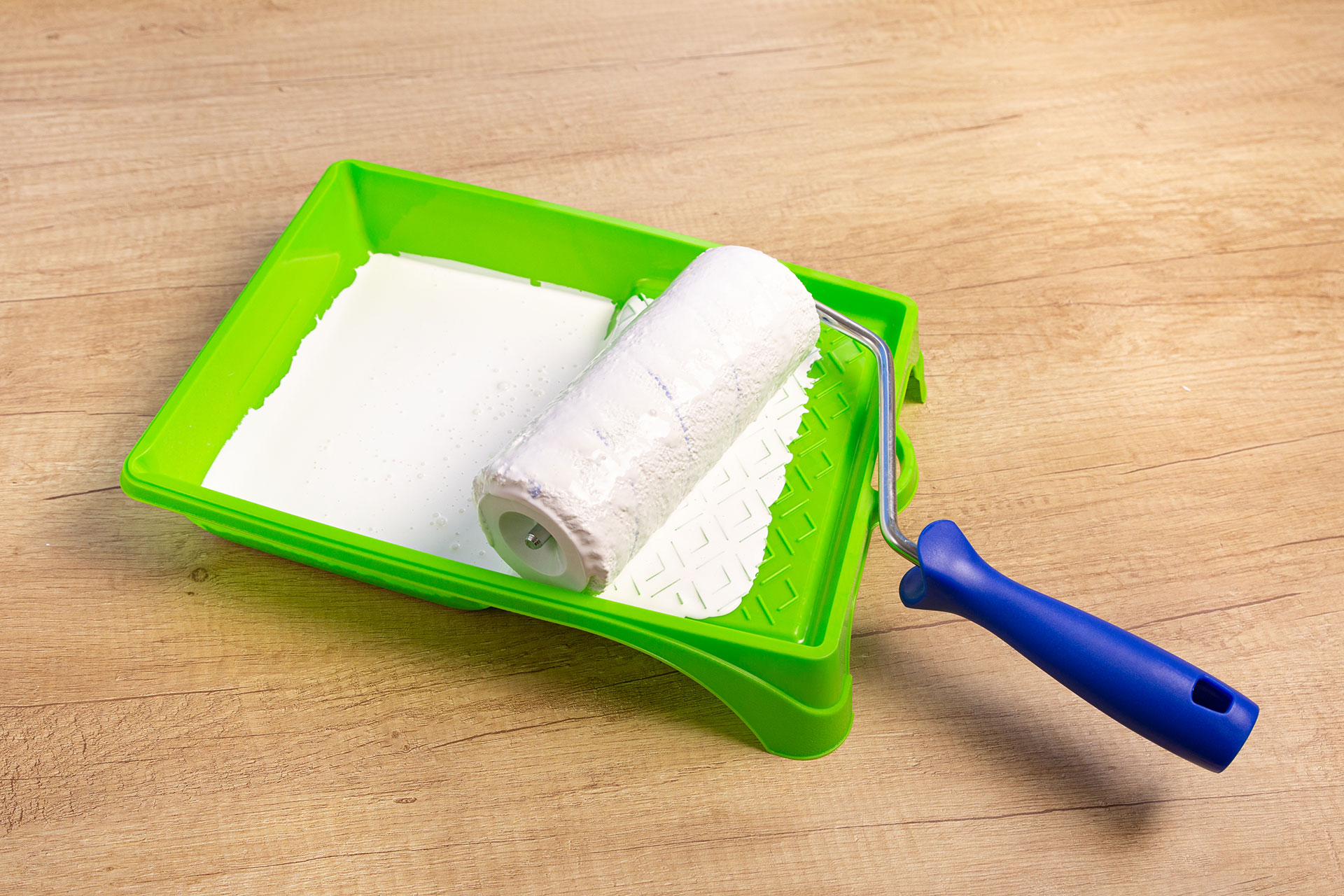 paint roller in a green tray with white paint