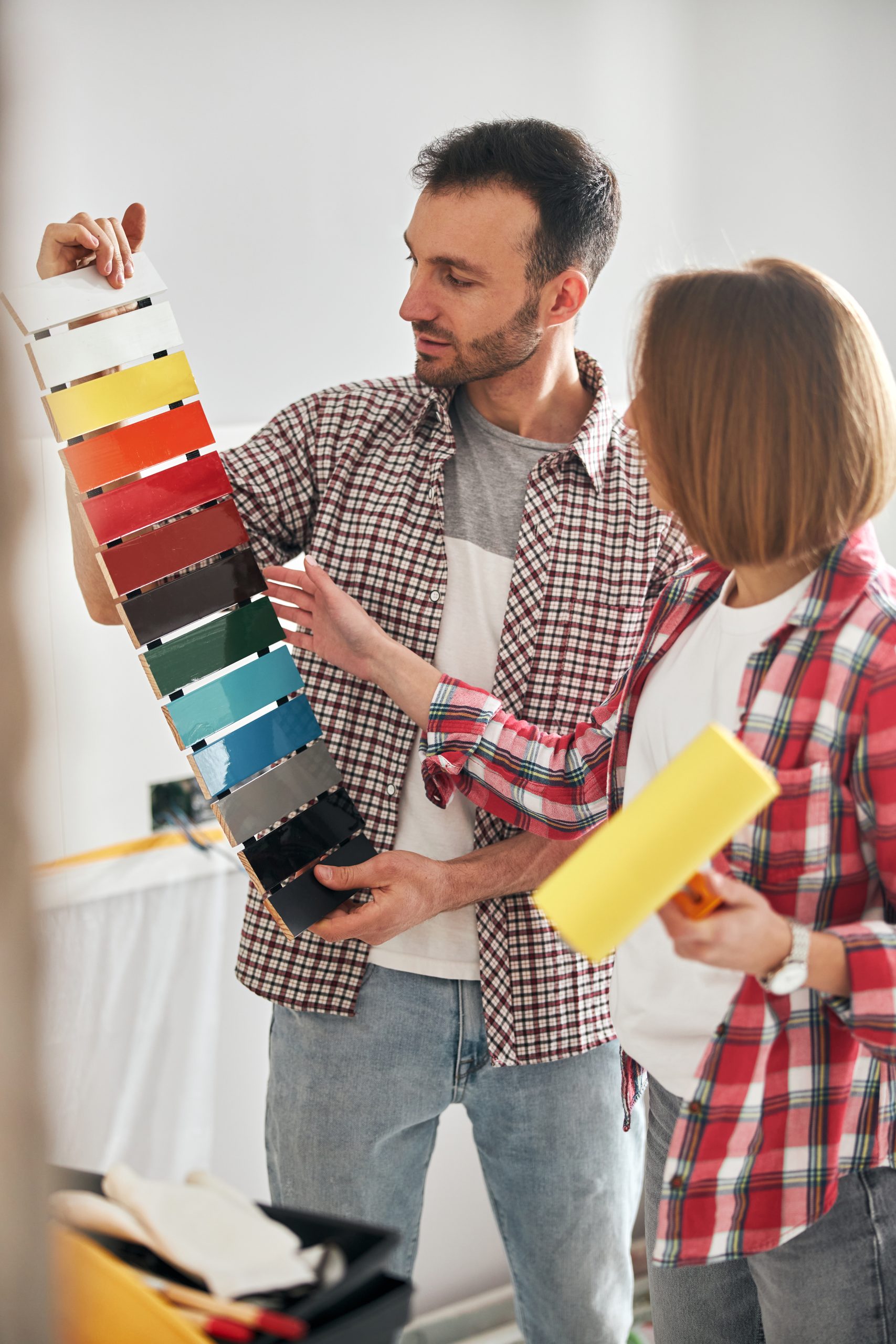 Bearded man holding a colored medium-density fiberboard sample kit in front of a female painter