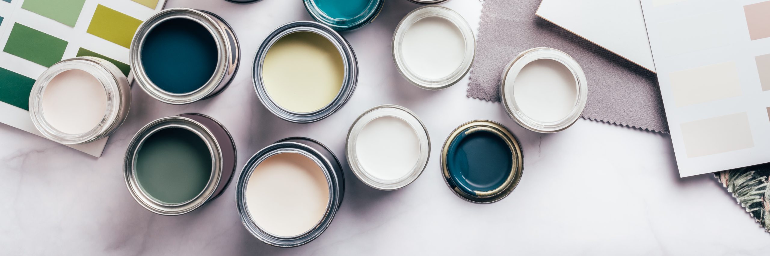Tiny sample paint cans during house renovation, process of choosing paint for the walls, different green and beige colors, color charts on background, banner size