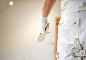 Painter holding brush, wearing white work clothes.